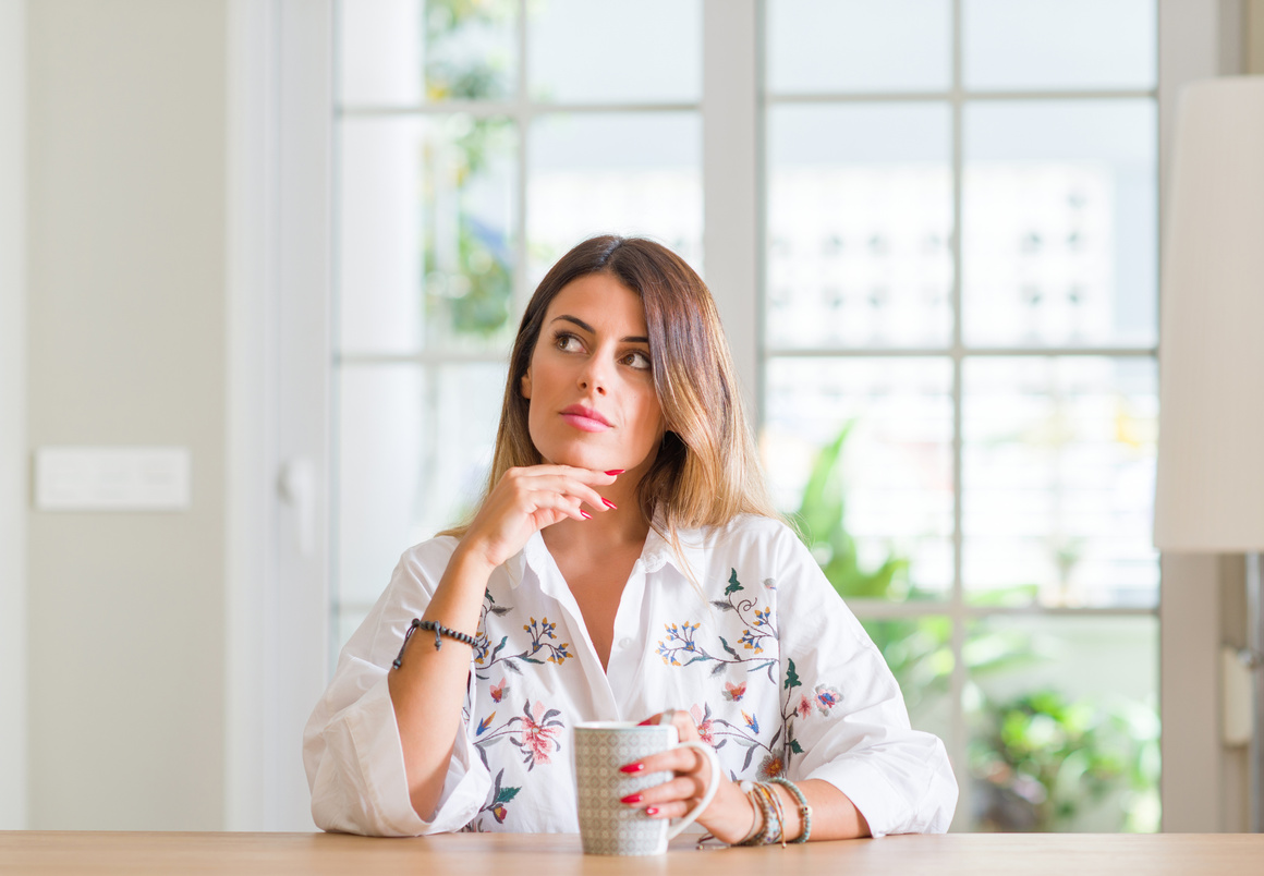 Young woman at home drinking coffee serious face thinking about question, very confused idea